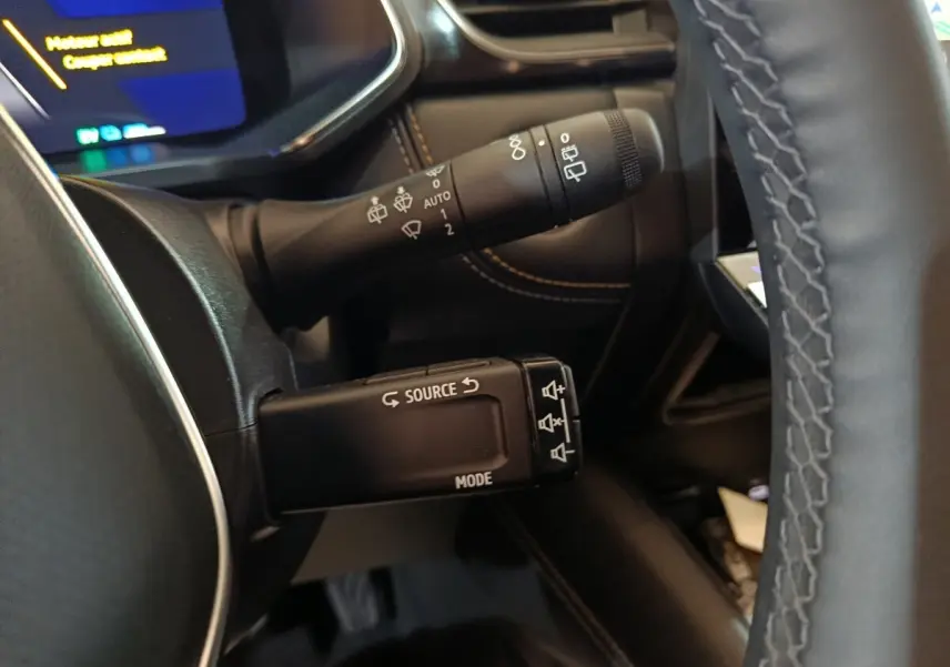 Gros plan sur les commandes au volant noir et les coutures marron du tableau de bord du Renault Symbioz bleu 2025.