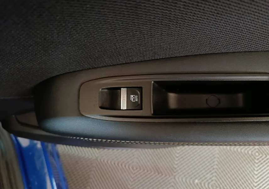 Gros plan sur la commande de lève-vitre côté gauche d'une Renault Symbioz bleu, intérieur tissu noir.