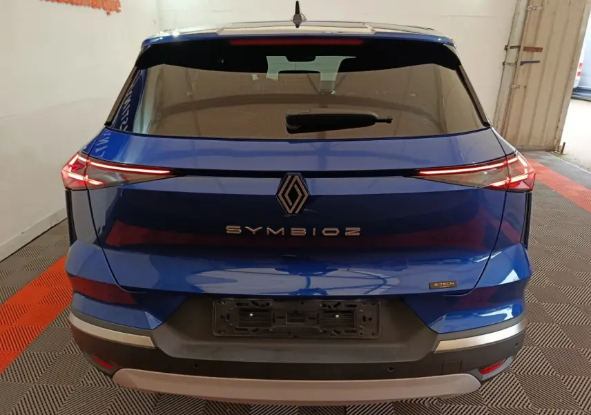 Vue arrière d'une Renault Symbioz bleu avec feux LED fins et logo central distinctif sur un fond intérieur.