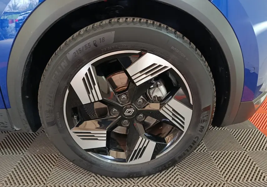 Gros plan sur la roue avant droite bleu Renault Symbioz 2025 avec jante noire et argent au design géométrique.