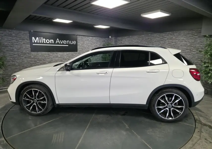 Vue de profil côté gauche d'un Mercedes GLA blanc avec jantes alliage 19 pouces bicolores dans un showroom.