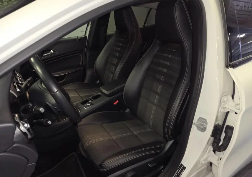 Vue intérieure côté conducteur du Mercedes GLA blanc, mettant en valeur les sièges sport noirs avec surpiqûres contrastées.