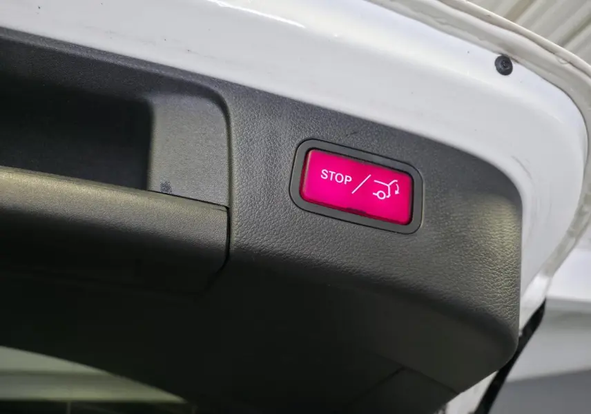 Détail du bouton stop rouge pour hayon électrique sur la partie intérieure du coffre d'un Mercedes GLA blanc.