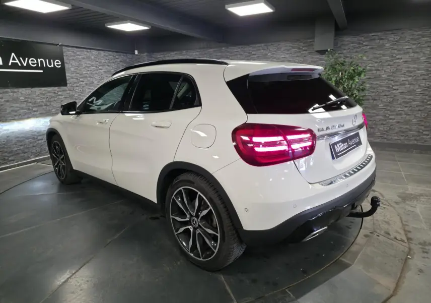 Vue 3/4 arrière droite d'un Mercedes GLA blanc avec jantes alliage noires et attelage démontable en intérieur showroom.