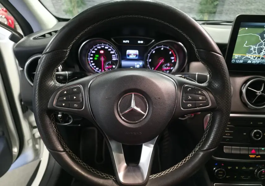 Vue centrée sur le volant en cuir perforé avec surpiqûres contrastées du Mercedes GLA blanc, tableau de bord et écran de navigation visibles.