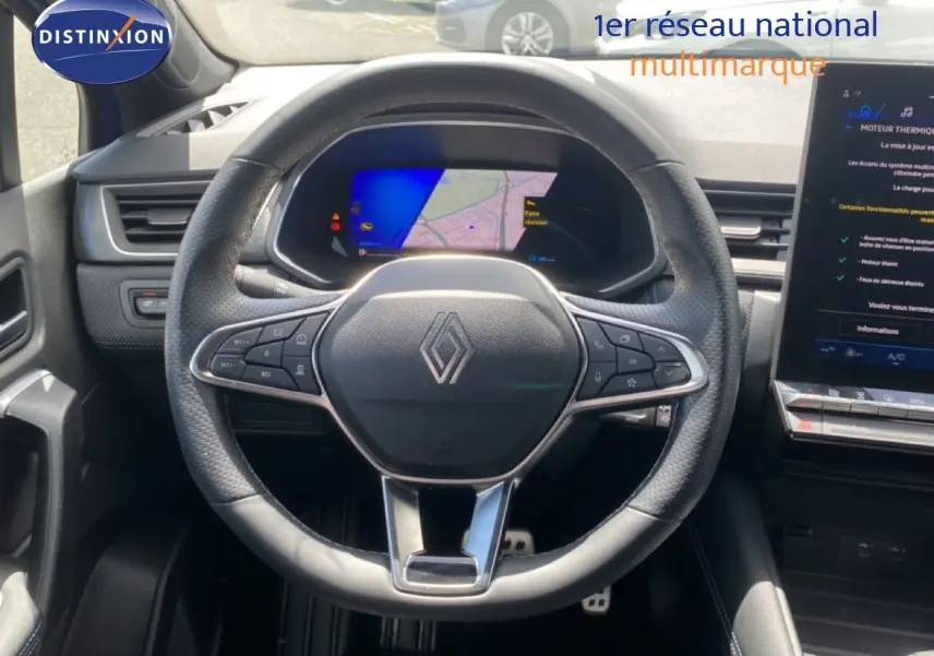 Vue intérieure centrée sur le volant perforé Renault Symbioz 2025 avec tableau de bord numérique et écran tactile adjacent.