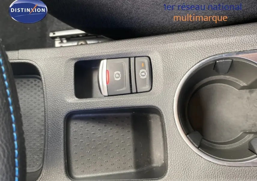 Gros plan sur la console centrale noire avec boutons de frein à main électronique et maintien auto, et porte-gobelet circulaire.