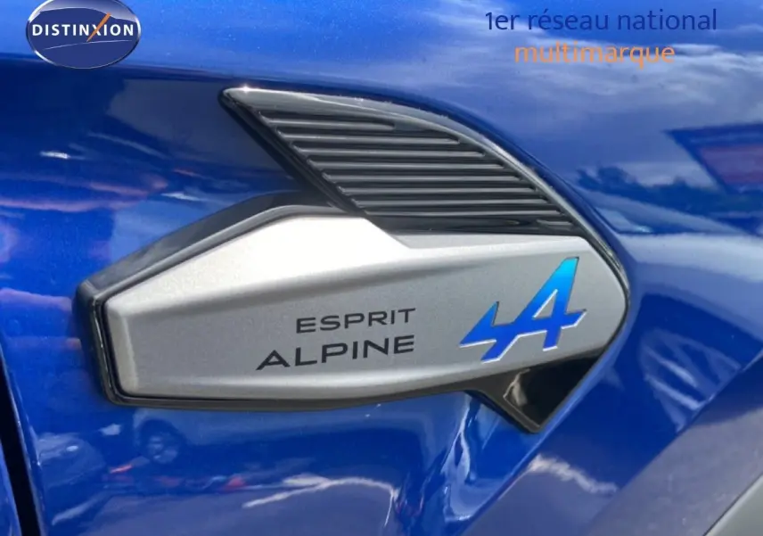 Gros plan sur l'emblème Esprit Alpine bleu sur la carrosserie bleu iron metal d'une Renault Symbioz hybride.