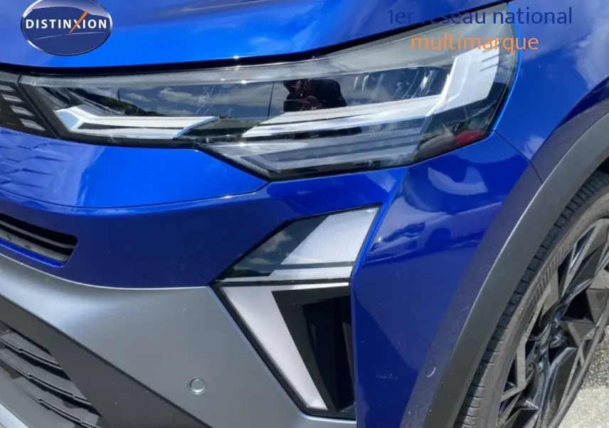 Gros plan sur l'avant droit bleu iron metal du Renault Symbioz E-Tech Full Hybrid, mettant en valeur le phare LED et la jante noire.