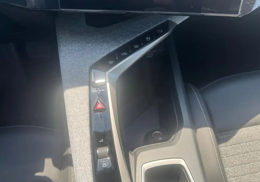 Vue plongeante sur la console centrale grise du Peugeot 5008 Hybrid 2025 avec commandes tactiles et rangement intégré.