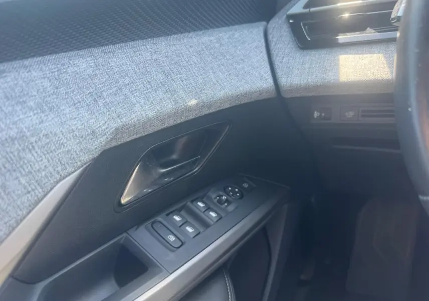 Détail de la porte côté conducteur du Peugeot 5008 Hybrid 2025, montrant les commandes des vitres et la garniture grise texturée.