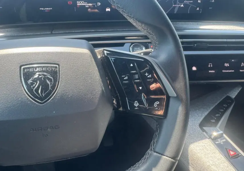 Vue rapprochée du volant noir du Peugeot 5008 Hybrid 2025 avec commandes tactiles et tableau de bord numérique.
