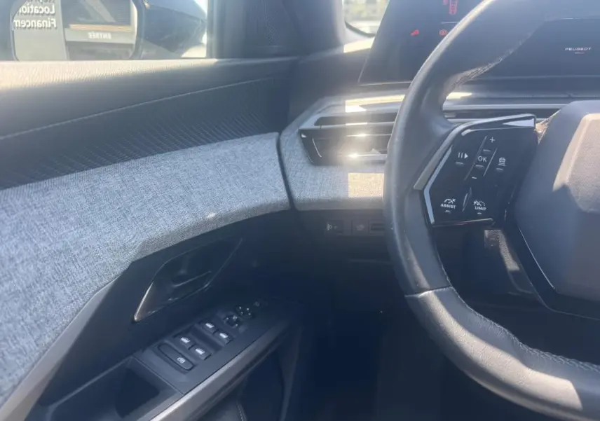 Intérieur du Peugeot 5008 Hybrid 2025, vue côté conducteur sur volant, commandes et panneau de porte gris clair.