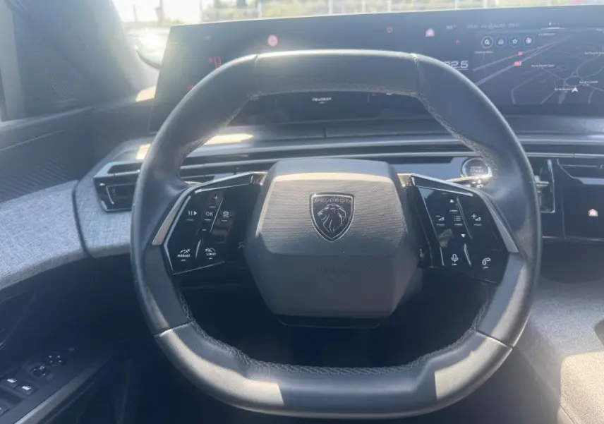Vue rapprochée du volant cuir noir du Peugeot 5008 Hybrid 2025, avec commandes intégrées et tableau de bord numérique.