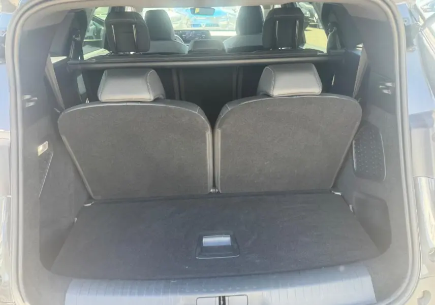 Coffre ouvert vu de l'arrière d'un Peugeot 5008 gris 2025 Hybrid Allure avec sièges arrière relevés.