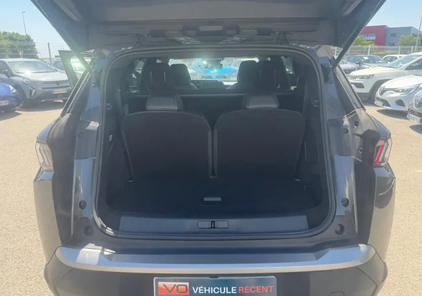 Coffre ouvert vu de l'arrière d'un Peugeot 5008 gris Hybrid 145 ch e-DCS6 Allure 2025 sur parking.
