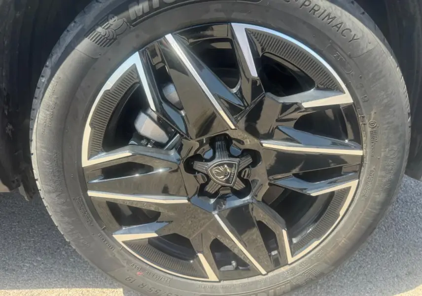 Gros plan sur la jante noire et argentée d’un Peugeot 5008 Hybrid gris, mettant en valeur le logo central et le pneu Michelin.