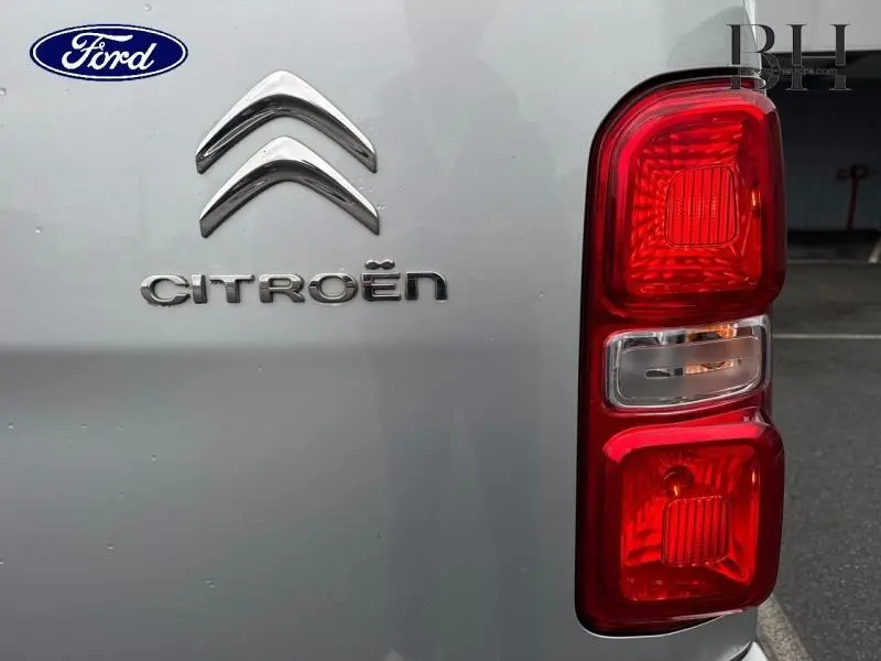 Gros plan sur le logo Citroën et le feu arrière droit d’un utilitaire gris aluminium.