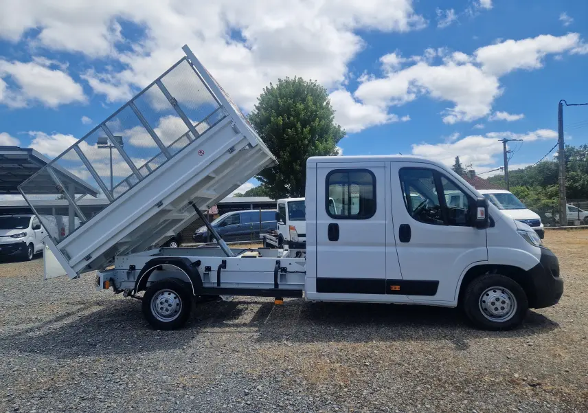 Vue latérale droite d'un Citroën Jumper blanc 2021 avec benne relevée et ridelles grillagées sur châssis double cabine.