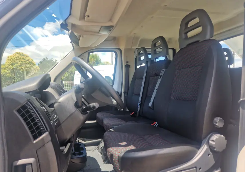 Intérieur du Citroën Jumper L3 blanc, vue côté conducteur, montrant la cabine double avec trois sièges noirs à motifs rouges.
