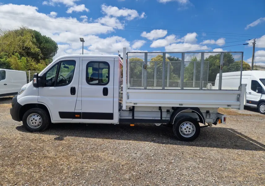 Vue de profil côté gauche d'un Citroën Jumper blanc avec double cabine et benne à ridelles grillagées.