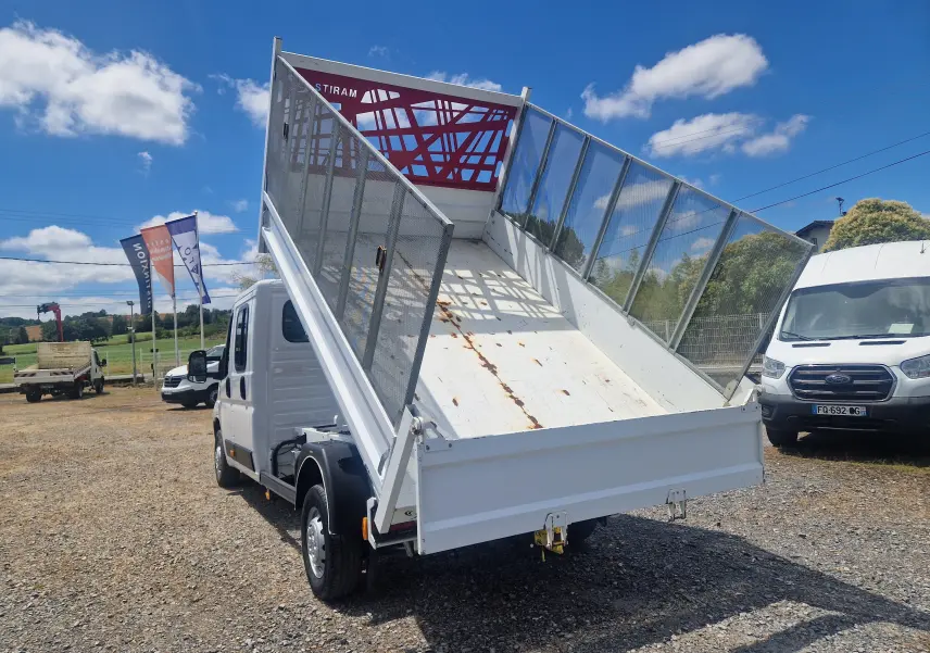 Citroën Jumper blanc vu 3/4 arrière avec benne relevée et ridelles grillagées sur côté droit.