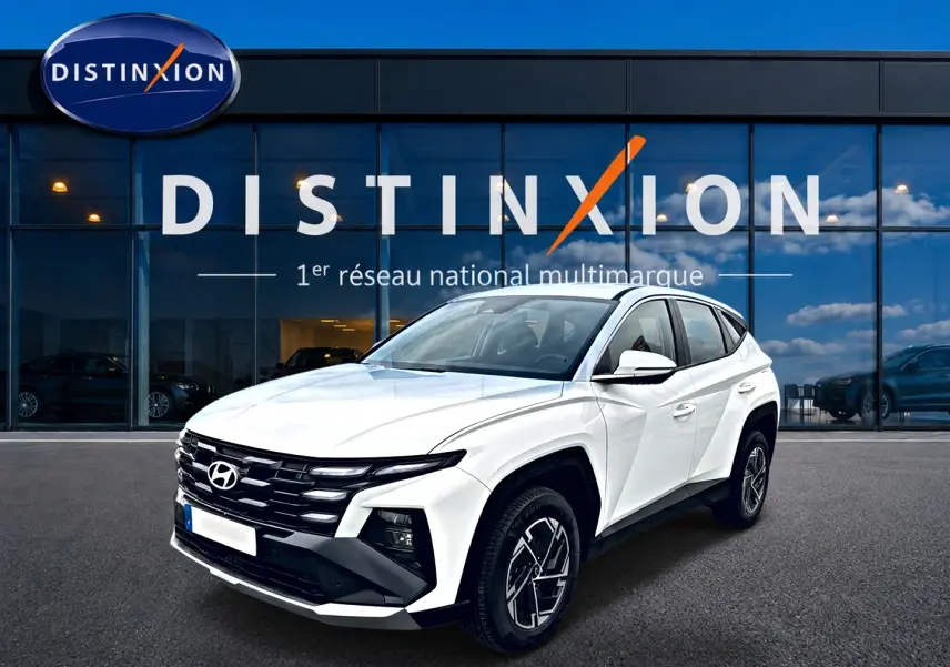 Vue 3/4 avant droite du Hyundai Tucson blanc 2026 avec calandre noire et jantes alliage 17 pouces devant un showroom Distinxion.
