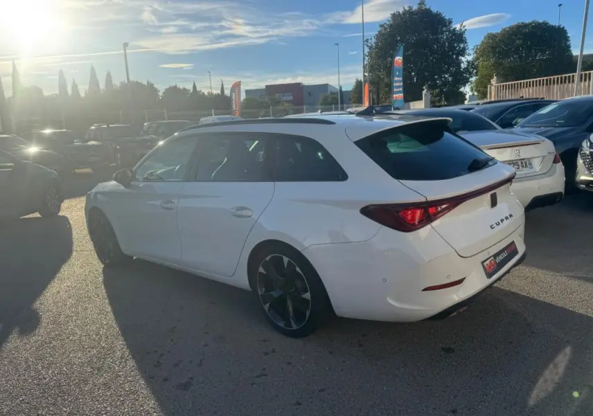 Vue 3/4 arrière droite d'une CUPRA Leon Sportstourer blanche 2024 avec jantes noires et toit ouvrant en extérieur.