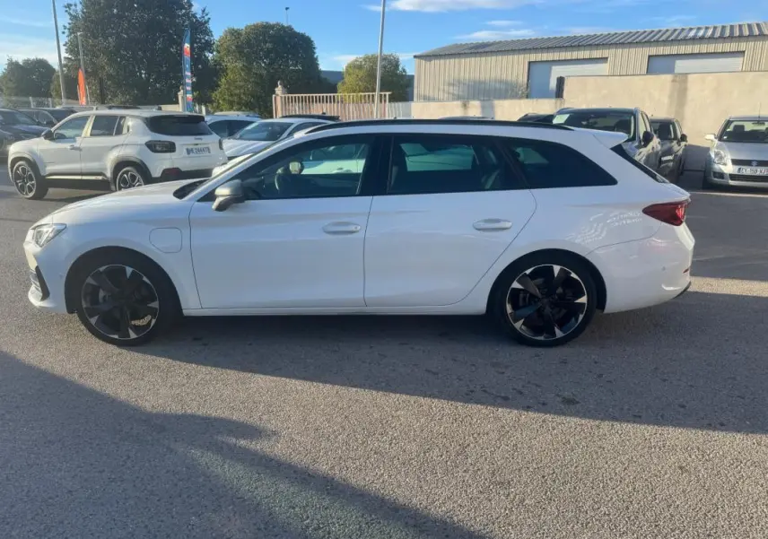 Vue de profil côté gauche d'une CUPRA Leon Sportstourer blanche 2024 avec jantes noires et prise de recharge hybride visible.