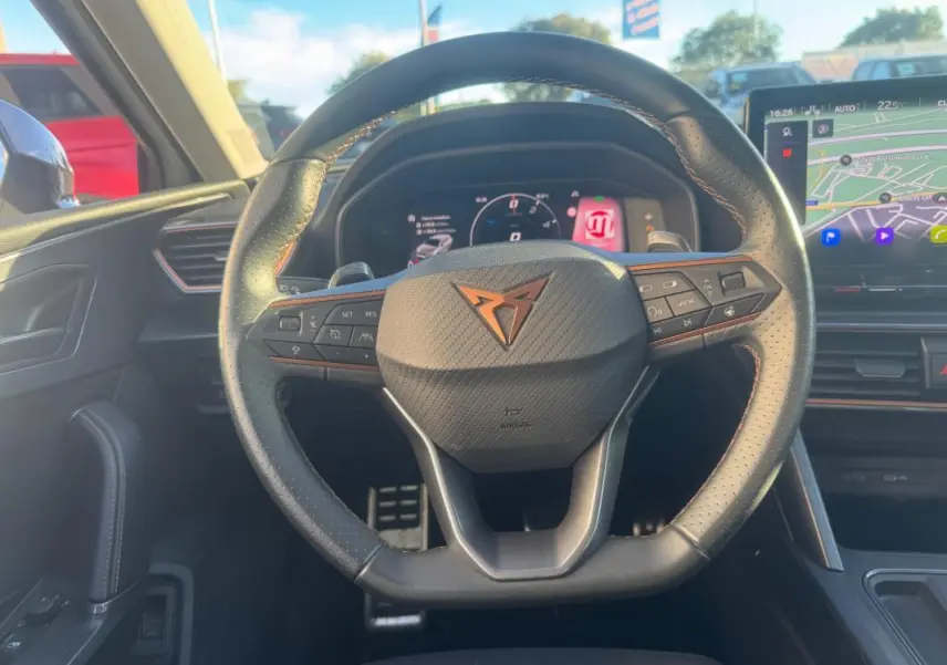 Vue intérieure centrée sur le volant noir perforé avec logo CUPRA cuivré, tableau de bord digital et écran tactile visible.