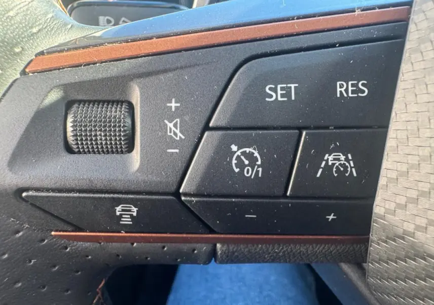 Gros plan sur les commandes noires du volant de la CUPRA Leon Sportstourer blanc, avec boutons de régulateur de vitesse et assistance.