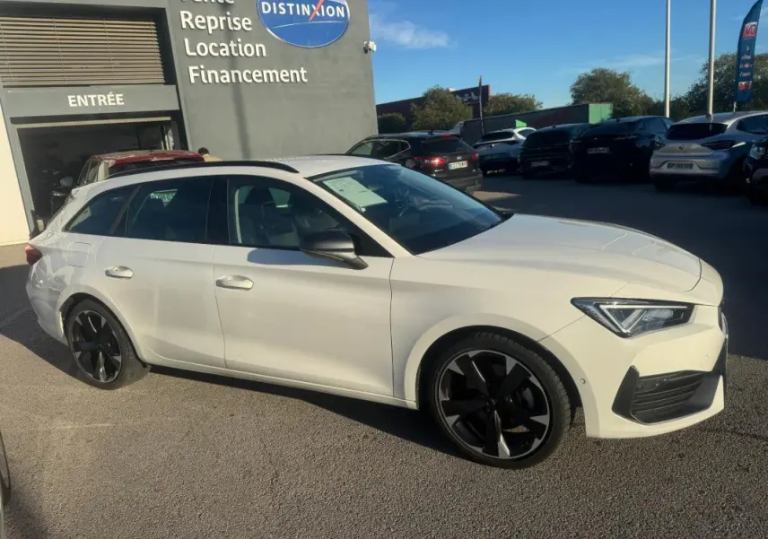 Vue 3/4 avant droite d'une CUPRA Leon Sportstourer blanche 2024 avec jantes noires et toit noir, stationnée en extérieur.