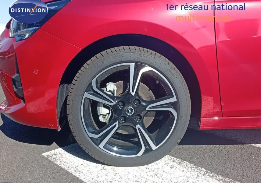 Gros plan sur la roue avant gauche d’une Opel Corsa rouge Kardio métal avec jante noire et détails argentés.