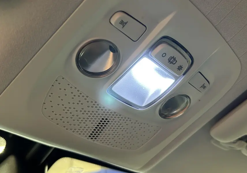 Vue en gros plan du plafonnier intérieur allumé du Peugeot 2008 blanc, avec commandes d’éclairage et haut-parleur intégré.