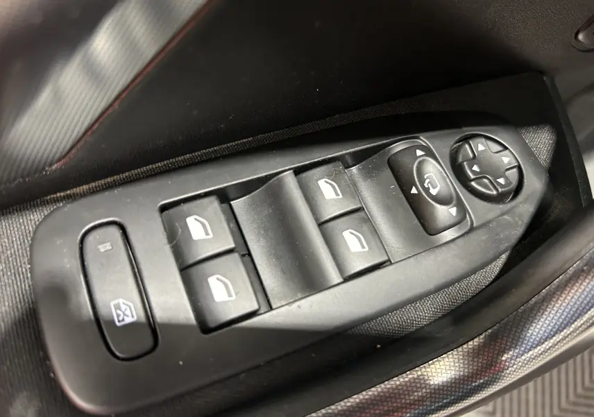 Gros plan sur les commandes des vitres électriques et rétroviseurs côté conducteur d'un Peugeot 2008 blanc de 2014.