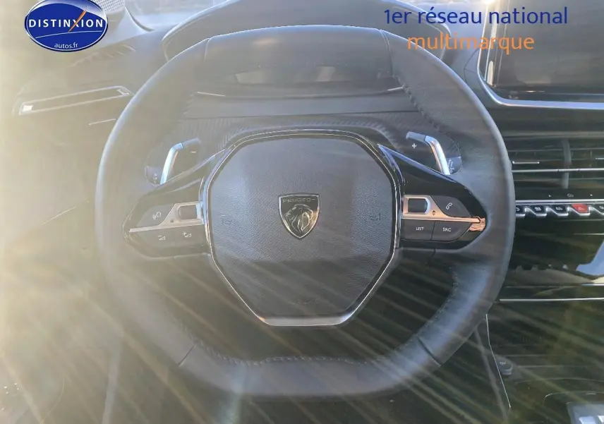 Vue rapprochée du volant noir de la Peugeot 208 1.2 hybrid 110 allure 2025 avec commandes intégrées.