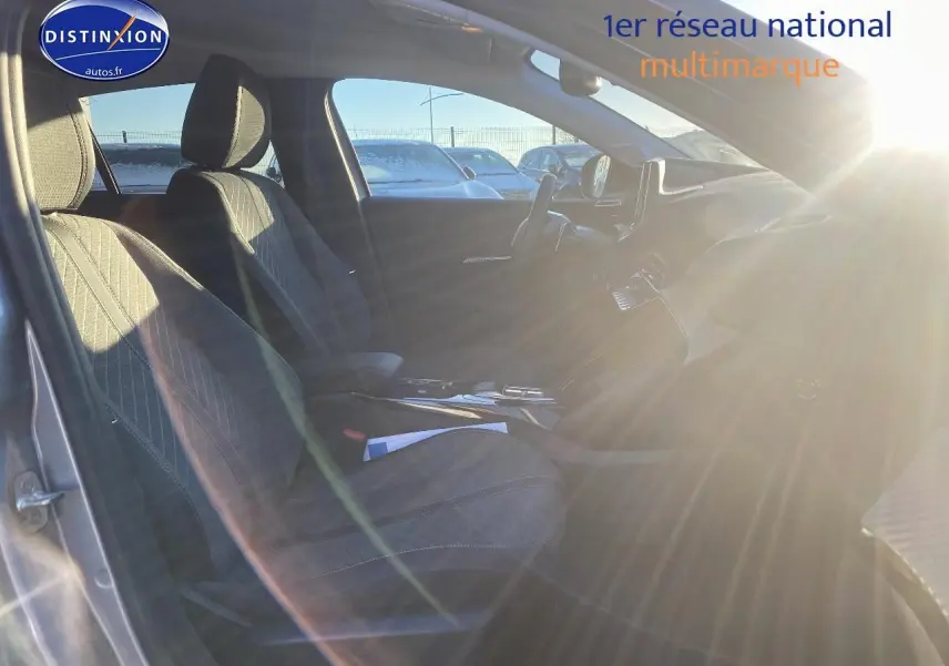 Intérieur avant droit de la Peugeot 208 gris artense 2025, sièges tissu avec accoudoir central et tableau de bord moderne.
