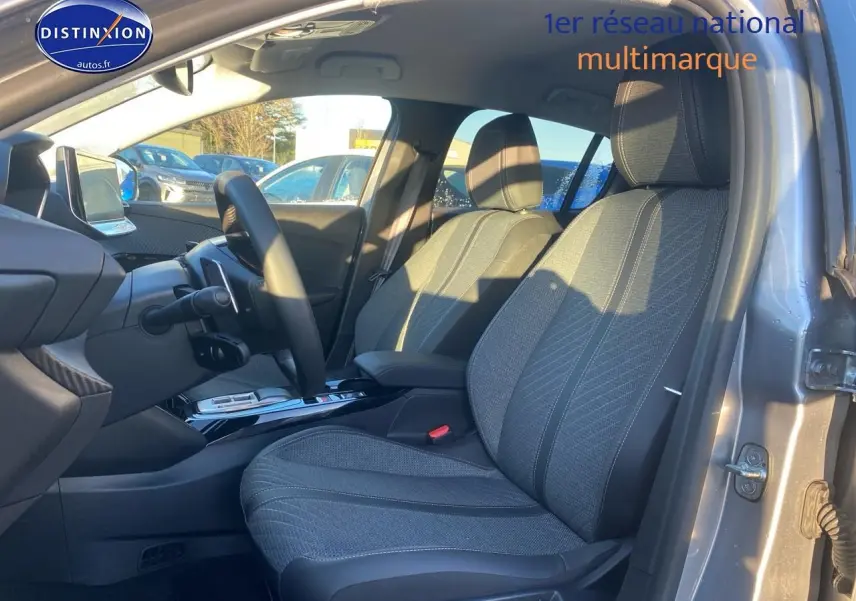 Vue intérieure côté conducteur de la Peugeot 208 gris artense, montrant les sièges avant et le volant.