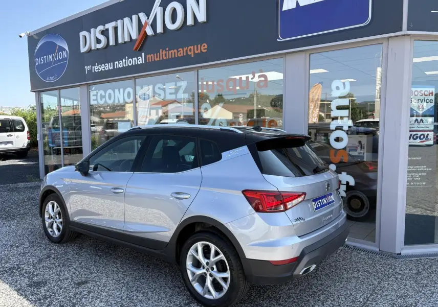Vue 3/4 arrière droite d'une SEAT Arona 2024 gris clair avec toit noir et jantes alliage 16 pouces devant un showroom.