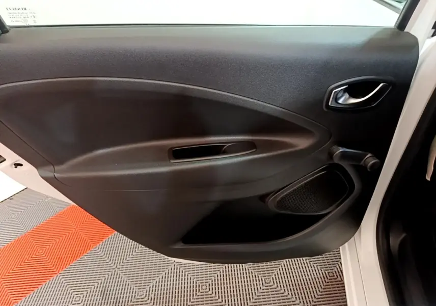 Vue intérieure de la porte avant gauche noire d'une Renault ZOE blanche, avec poignée et haut-parleur intégrés.