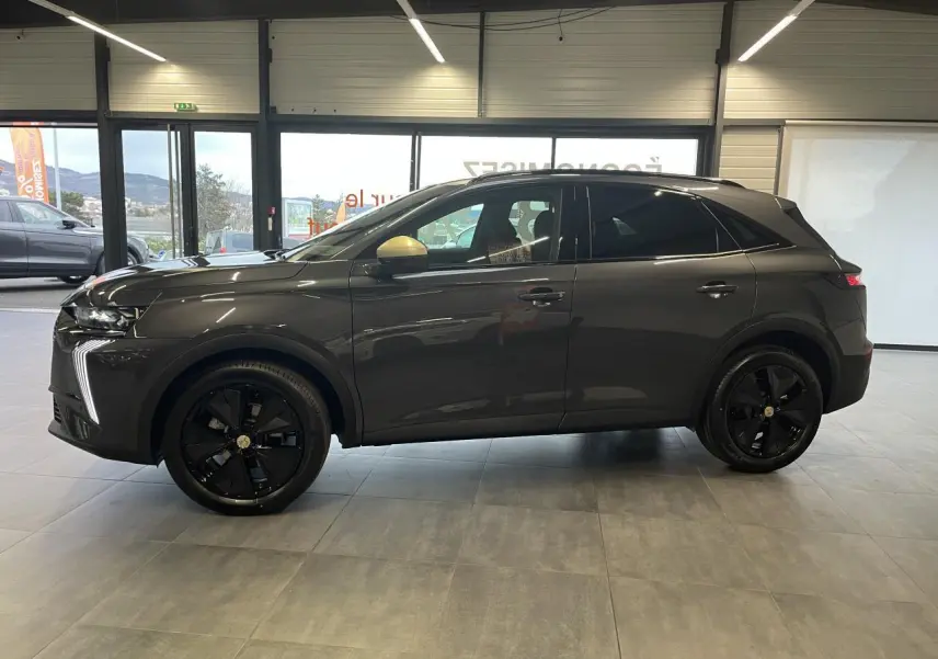 DS7 Crossback gris titanium vu de profil côté gauche en intérieur, avec jantes noires et rétroviseurs dorés.