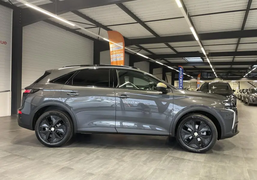 Vue latérale droite du DS7 Crossback gris titanium avec jantes noires et barres de toit noir brillant en intérieur showroom.