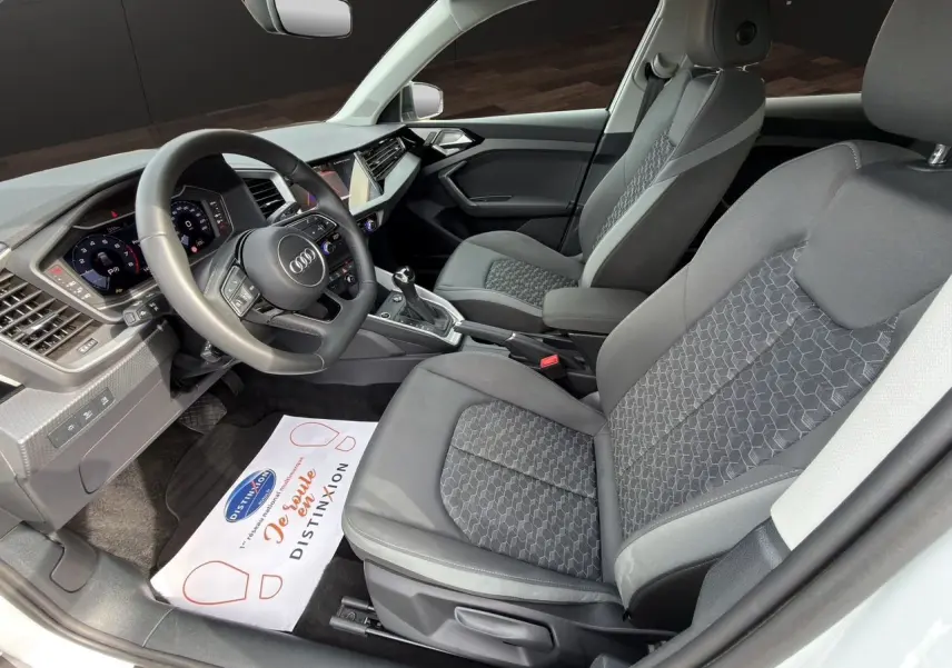 Vue intérieure côté conducteur de l’Audi A1 Sportback 2025 avec sièges tissu noir et tableau de bord moderne.
