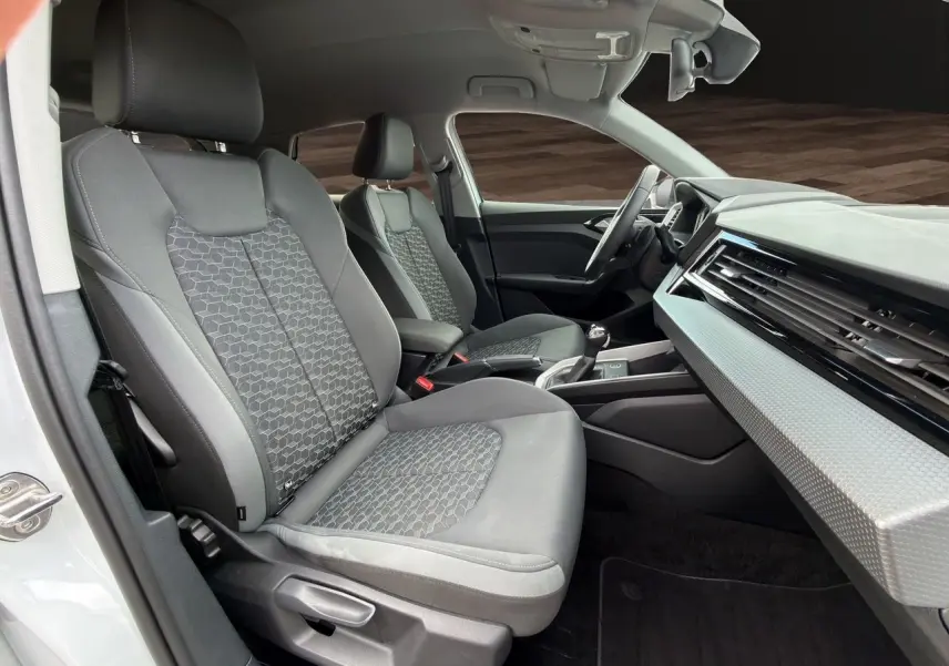Vue intérieure côté conducteur de l'Audi A1 Sportback 2025 avec sièges tissu gris et tableau de bord clair.