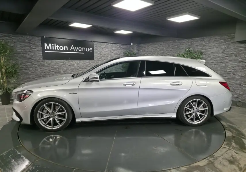 Vue de profil côté gauche d'une Mercedes CLA Shooting Brake 45 AMG gris métallisé en intérieur showroom.