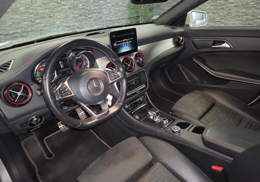 Vue intérieure côté conducteur de la Mercedes CLA Shooting Brake 45 AMG avec volant cuir perforé et finitions rouges.