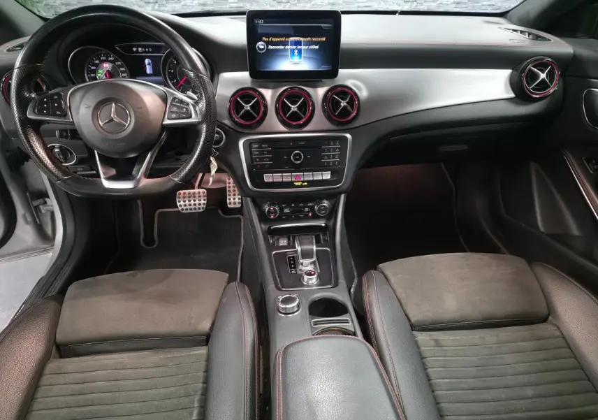Vue intérieure avant de la Mercedes CLA Shooting Brake 45 AMG avec tableau de bord noir et aérateurs cerclés de rouge.