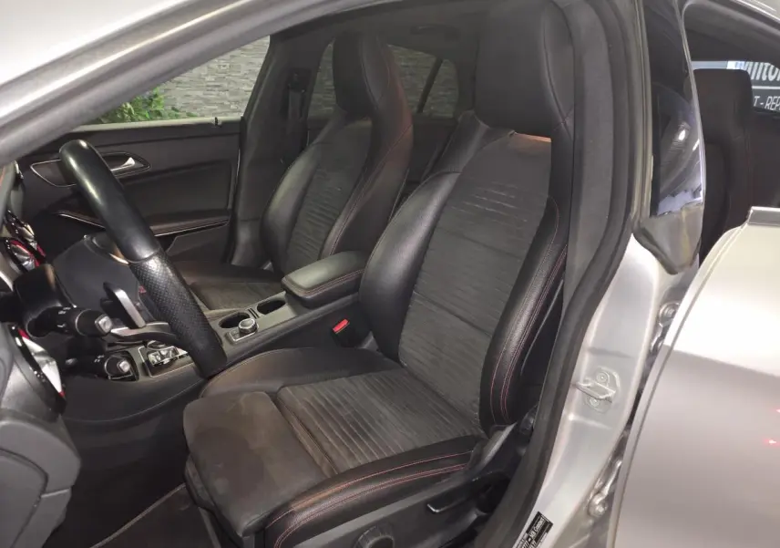 Vue intérieure côté conducteur d'une Mercedes CLA Shooting Brake grise, sièges sport en cuir noir avec surpiqûres rouges.
