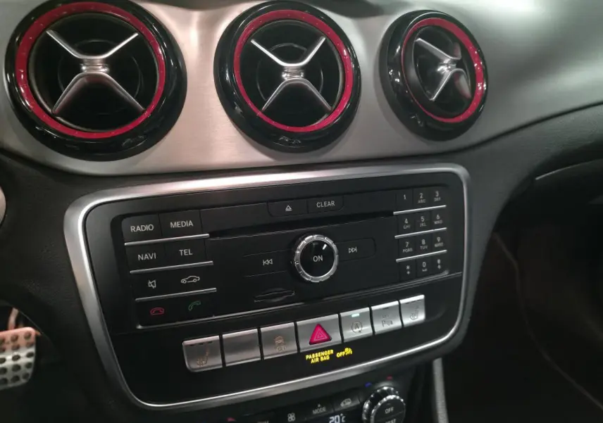 Détail du tableau de bord de la Mercedes CLA Shooting Brake 45 AMG 2016 avec aérateurs ronds à contour rouge et console centrale noire.