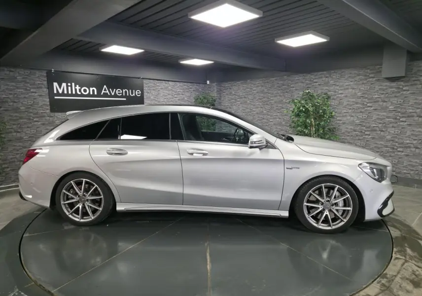 Vue de profil côté gauche d'une Mercedes Classe CLA Shooting Brake gris métallisé avec jantes AMG 18 pouces en intérieur showroom.